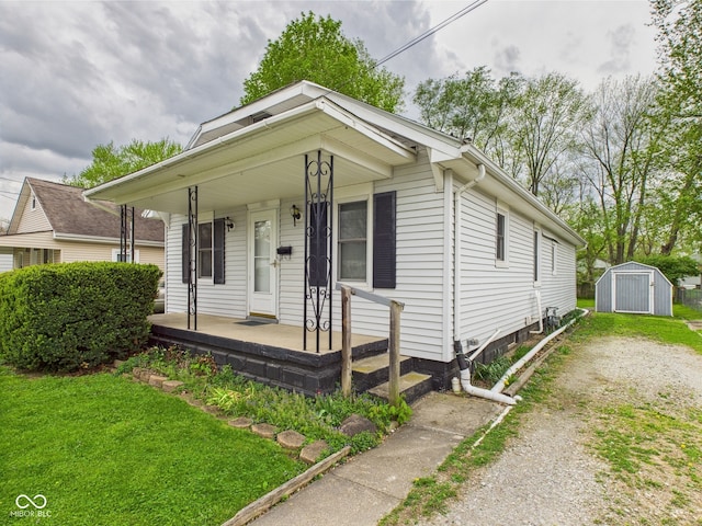view of front of property with a front lawn, covered porch, driveway, a shed, and an outbuilding