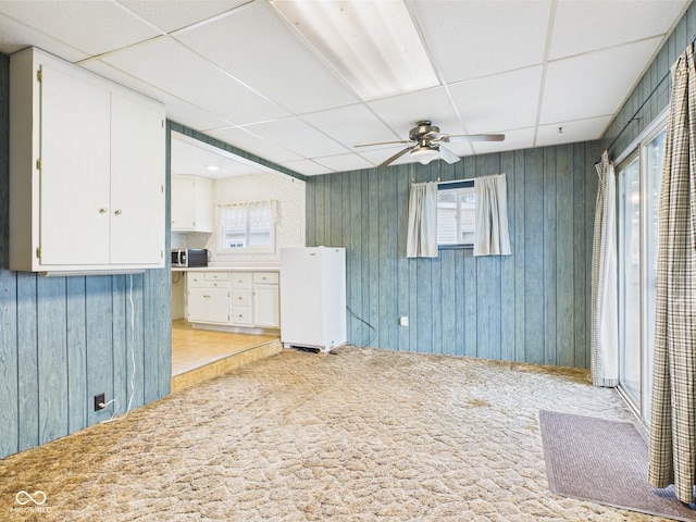 interior space with ceiling fan, a drop ceiling, and light carpet