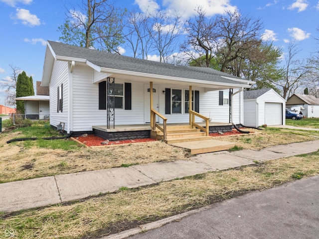 bungalow with a detached garage, covered porch, a shingled roof, and an outbuilding