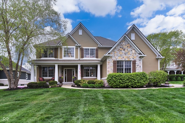 craftsman-style house with a porch, a shingled roof, a front yard, and stone siding
