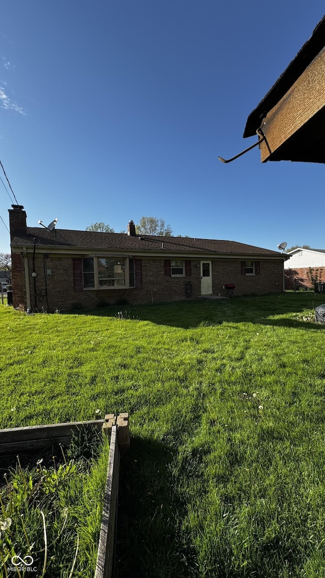 back of property featuring a lawn, brick siding, and a chimney