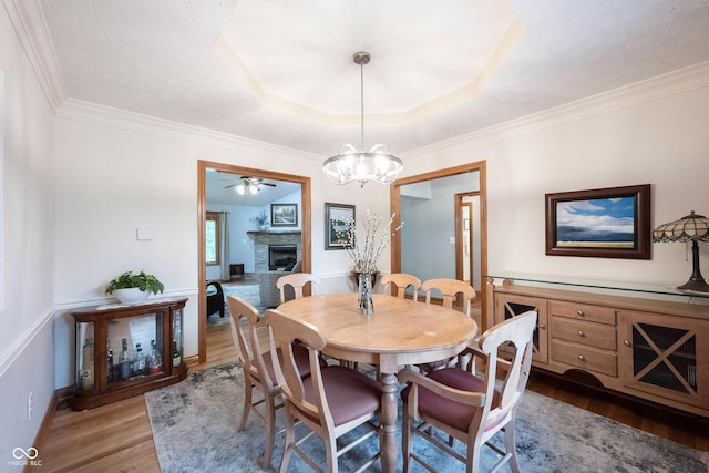 dining space featuring a tray ceiling, ornamental molding, a chandelier, wood finished floors, and a fireplace