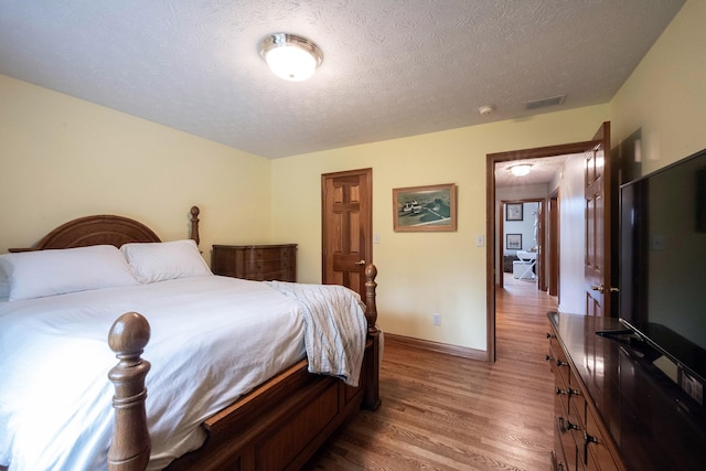 bedroom with light wood-style floors, visible vents, baseboards, and a textured ceiling