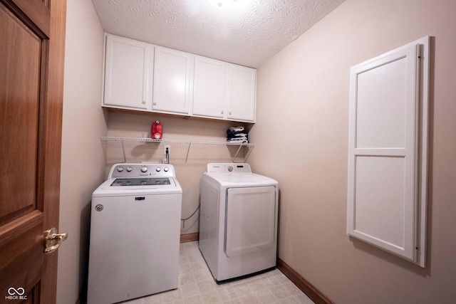 clothes washing area with washer and clothes dryer, a textured ceiling, cabinet space, and baseboards