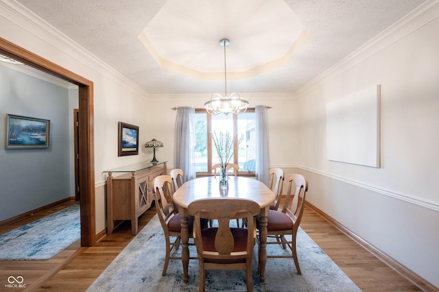 dining space with an inviting chandelier, a raised ceiling, baseboards, and wood finished floors