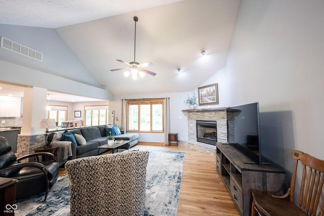 living room with a ceiling fan, a stone fireplace, light wood finished floors, visible vents, and high vaulted ceiling