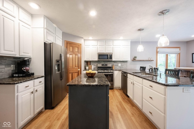 kitchen featuring a peninsula, a sink, stainless steel appliances, white cabinetry, and backsplash