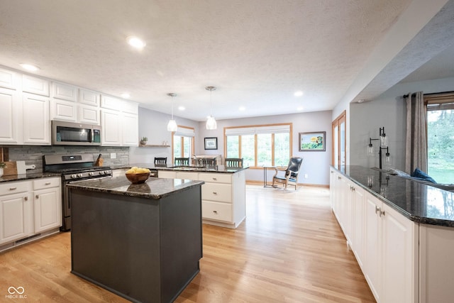 kitchen with a peninsula, light wood-type flooring, recessed lighting, a center island, and appliances with stainless steel finishes