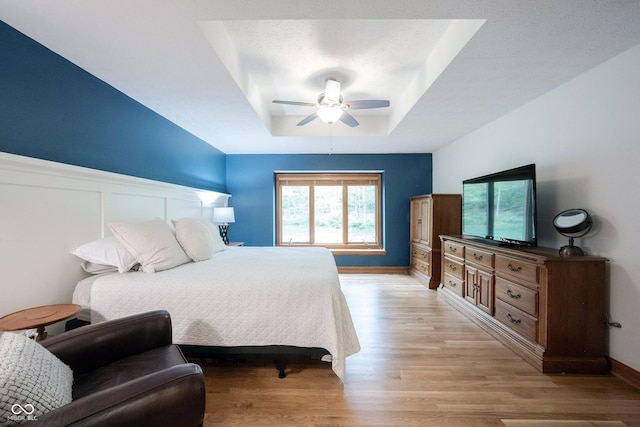 bedroom with light wood finished floors, a ceiling fan, baseboards, and a raised ceiling