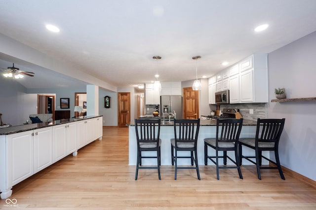kitchen with stainless steel appliances, a peninsula, light wood-style flooring, and white cabinets