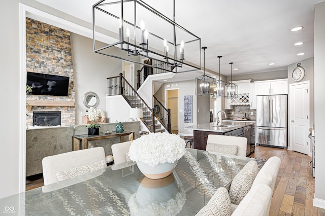 dining area featuring stairs, a fireplace, recessed lighting, hardwood / wood-style flooring, and a notable chandelier