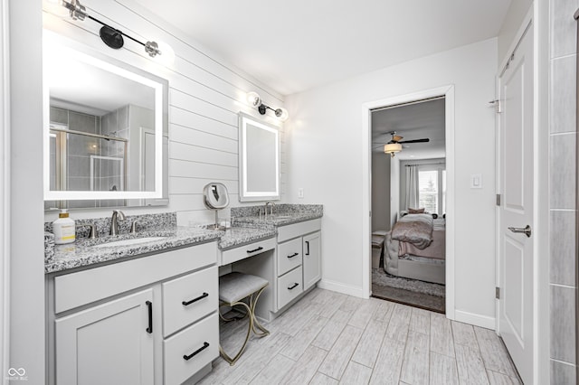 ensuite bathroom featuring double vanity, a sink, a ceiling fan, and a shower stall