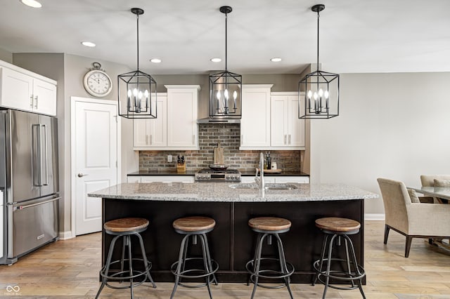 kitchen featuring a sink, baseboards, stainless steel appliances, light wood-style flooring, and an island with sink