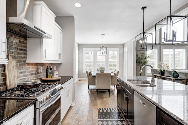 kitchen with white cabinets, a sink, light wood-style floors, wall chimney exhaust hood, and stainless steel appliances