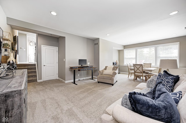 living area with stairway, baseboards, visible vents, and light colored carpet