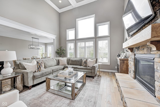 living room with crown molding, a towering ceiling, a stone fireplace, baseboards, and light wood-style flooring