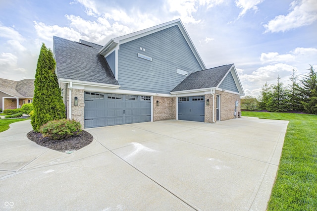 view of home's exterior with roof with shingles, brick siding, a garage, a yard, and driveway