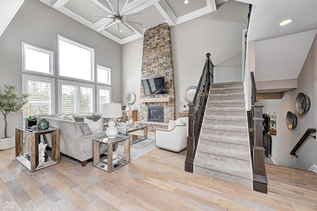 living area featuring a high ceiling, light wood finished floors, a fireplace, stairs, and coffered ceiling
