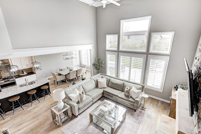 living room with light wood-style floors, baseboards, ceiling fan with notable chandelier, and a high ceiling