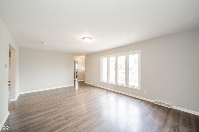 unfurnished living room with baseboards, visible vents, and dark wood-type flooring