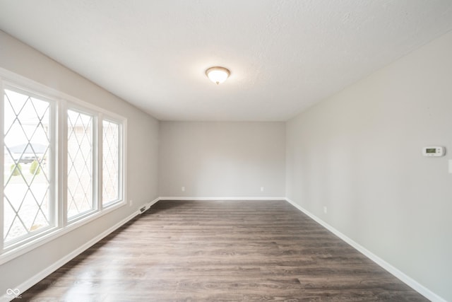 empty room with dark wood-type flooring, a textured ceiling, and baseboards