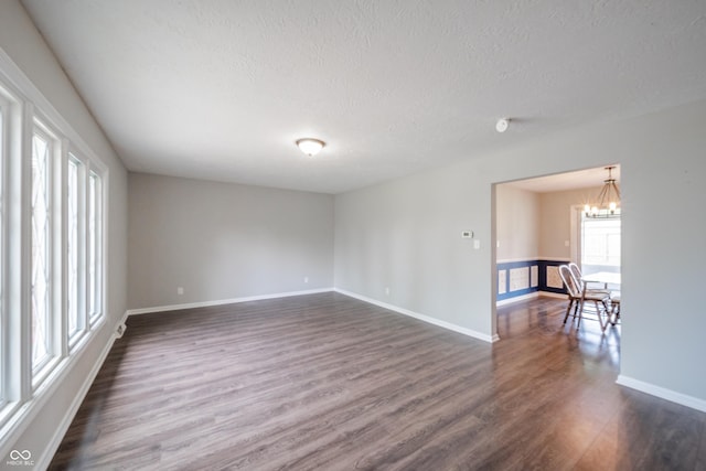unfurnished room with baseboards, a textured ceiling, a notable chandelier, and dark wood finished floors