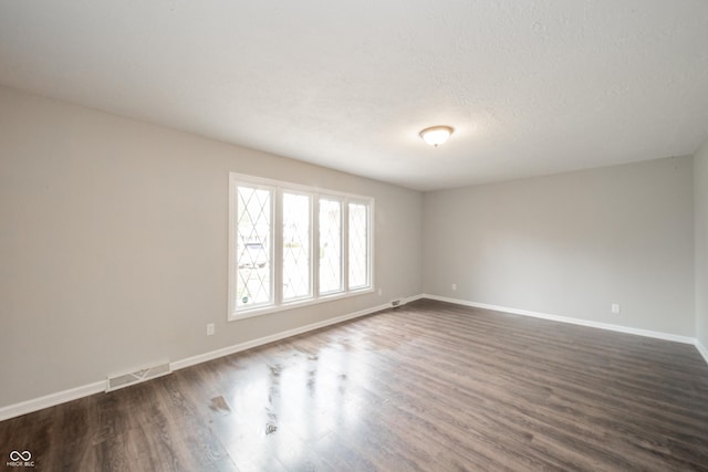 empty room with baseboards, dark wood-style floors, a textured ceiling, and visible vents