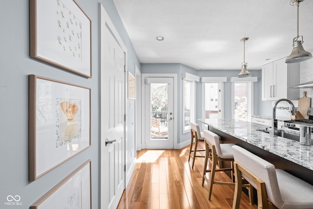 kitchen featuring pendant lighting, a kitchen breakfast bar, white cabinetry, light stone counters, and light wood-style flooring