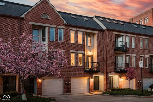 townhome / multi-family property with brick siding, driveway, a shingled roof, and a garage