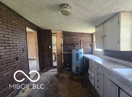 kitchen with brick wall, a textured ceiling, white cabinetry, a sink, and water heater