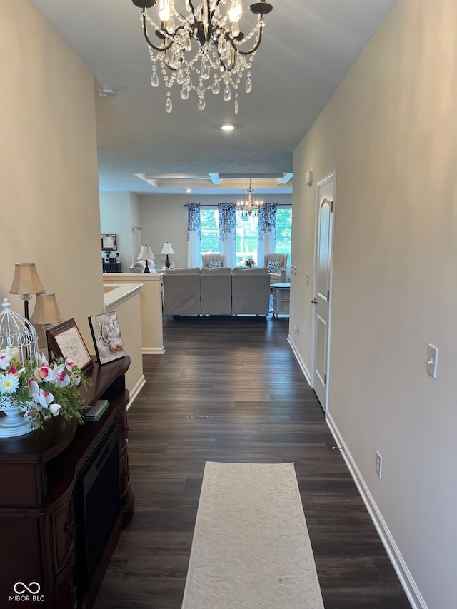 corridor featuring an inviting chandelier, baseboards, and dark wood-style flooring