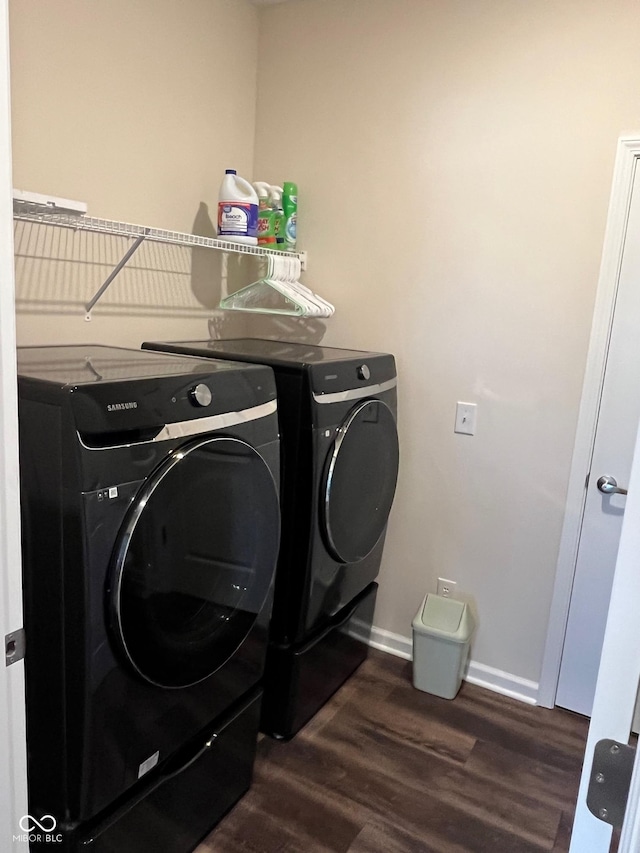 clothes washing area with laundry area, washing machine and dryer, baseboards, and dark wood-type flooring