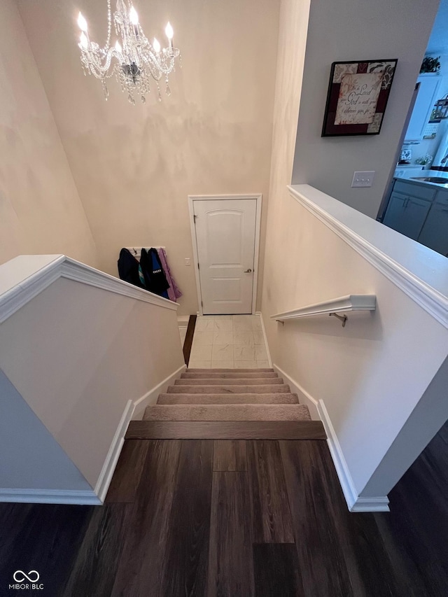 staircase with baseboards, an inviting chandelier, and wood finished floors