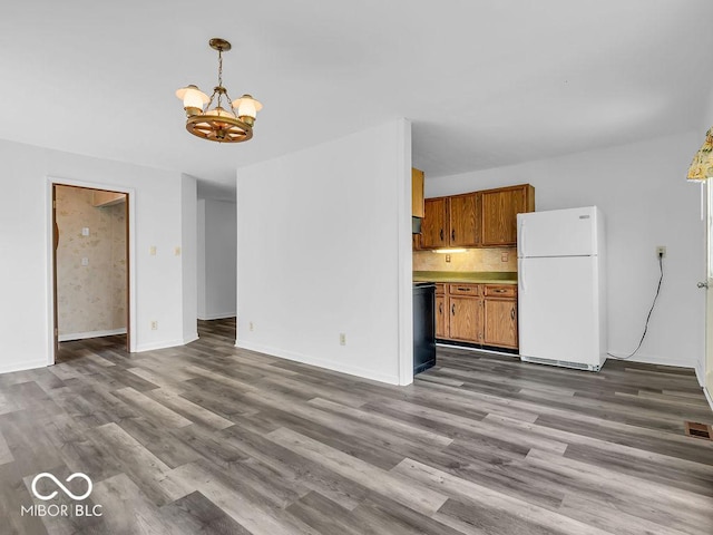 kitchen with freestanding refrigerator, brown cabinets, wood finished floors, and a chandelier