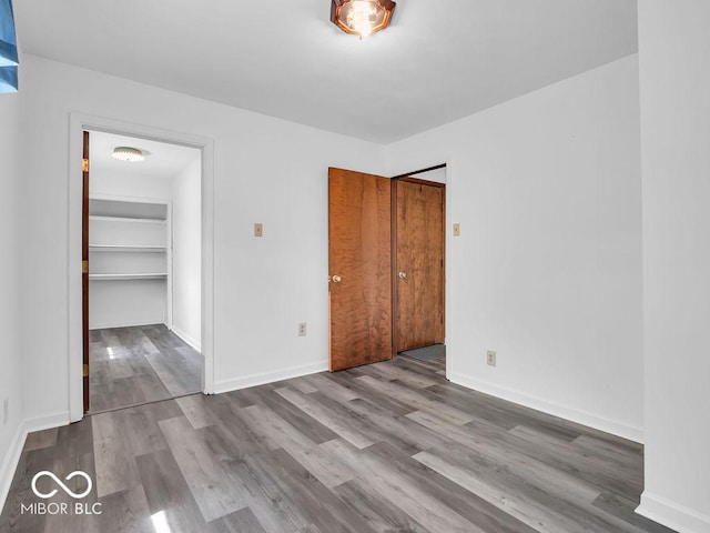 unfurnished bedroom with a walk in closet, baseboards, wood finished floors, and a closet