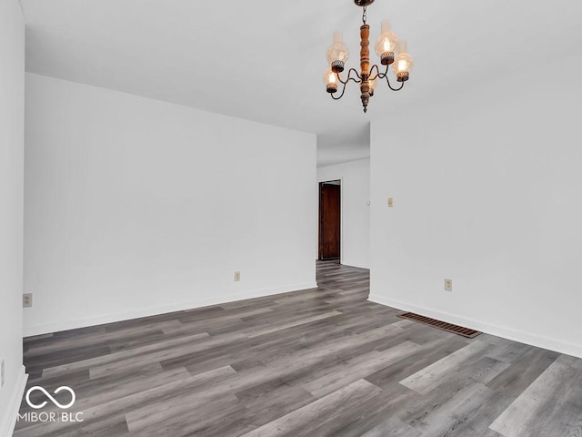 spare room featuring an inviting chandelier, baseboards, wood finished floors, and visible vents