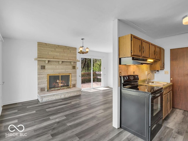 kitchen featuring brown cabinetry, electric range, wood finished floors, under cabinet range hood, and a sink