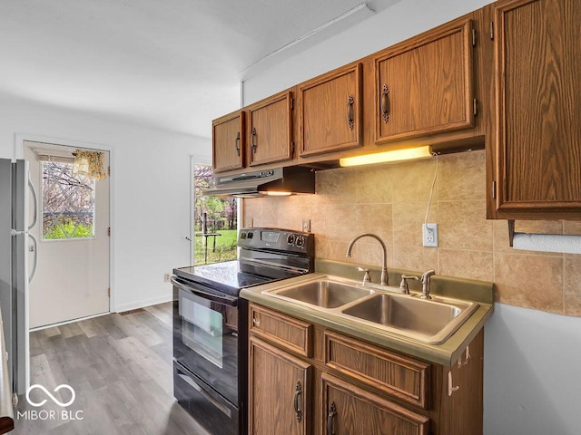 kitchen with tasteful backsplash, black range with electric stovetop, wood finished floors, a sink, and under cabinet range hood
