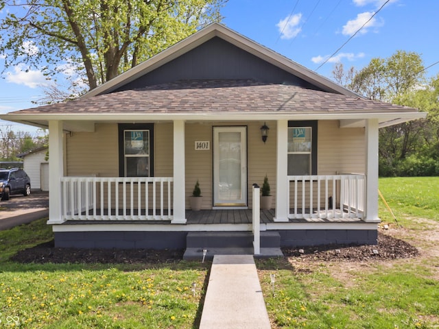 bungalow-style home with covered porch, a front yard, and roof with shingles