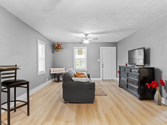 living area with baseboards, a textured ceiling, light wood finished floors, and a ceiling fan