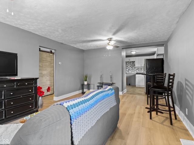 living room featuring ceiling fan, a barn door, a textured ceiling, light wood-style flooring, and visible vents