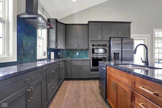 kitchen featuring appliances with stainless steel finishes, tasteful backsplash, vaulted ceiling, a sink, and dark stone countertops
