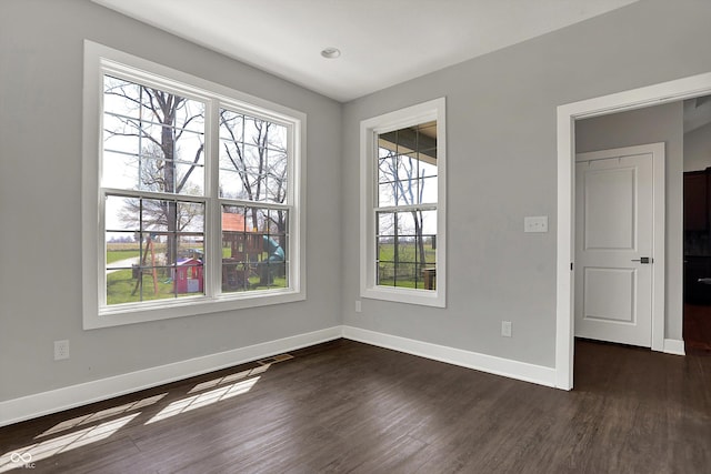 spare room featuring baseboards and dark wood-type flooring