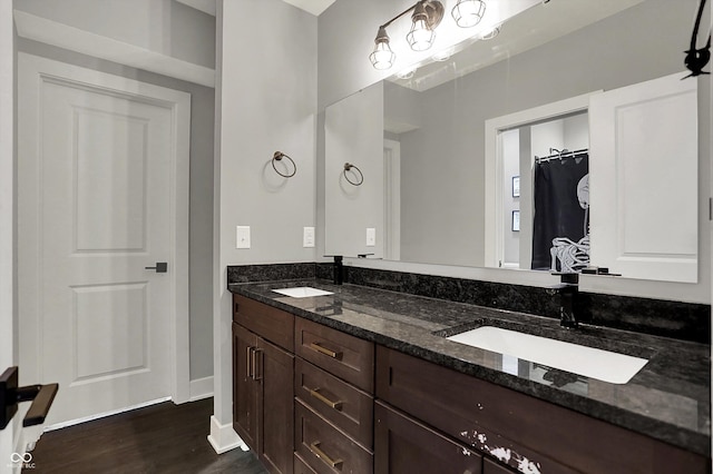 full bathroom with baseboards, a sink, wood finished floors, and double vanity