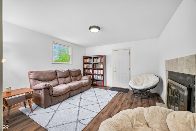 living room featuring a tiled fireplace, baseboards, and wood finished floors