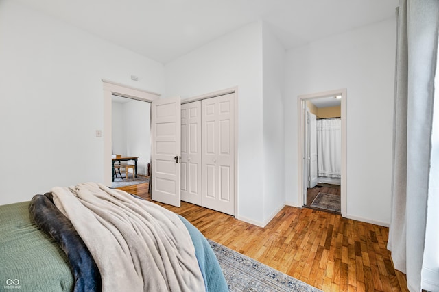 bedroom featuring baseboards, a closet, ensuite bath, and wood finished floors