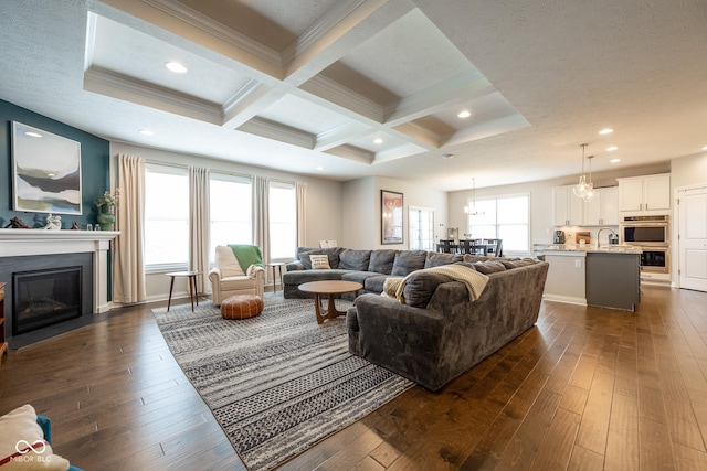 living area featuring a fireplace with flush hearth, ornamental molding, beamed ceiling, and dark wood-style floors