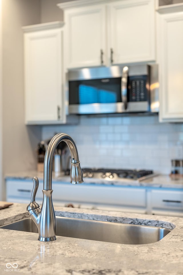 room details featuring white cabinetry, stainless steel microwave, a sink, and tasteful backsplash