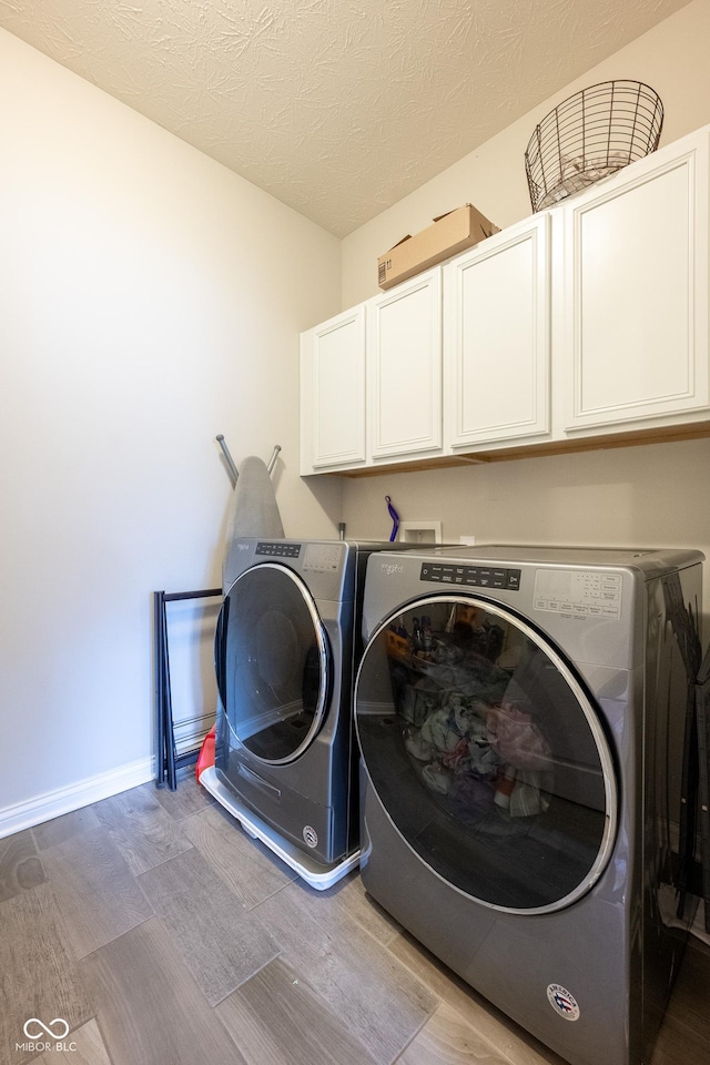 laundry area with cabinet space, a textured ceiling, light wood-style flooring, baseboards, and washer and clothes dryer