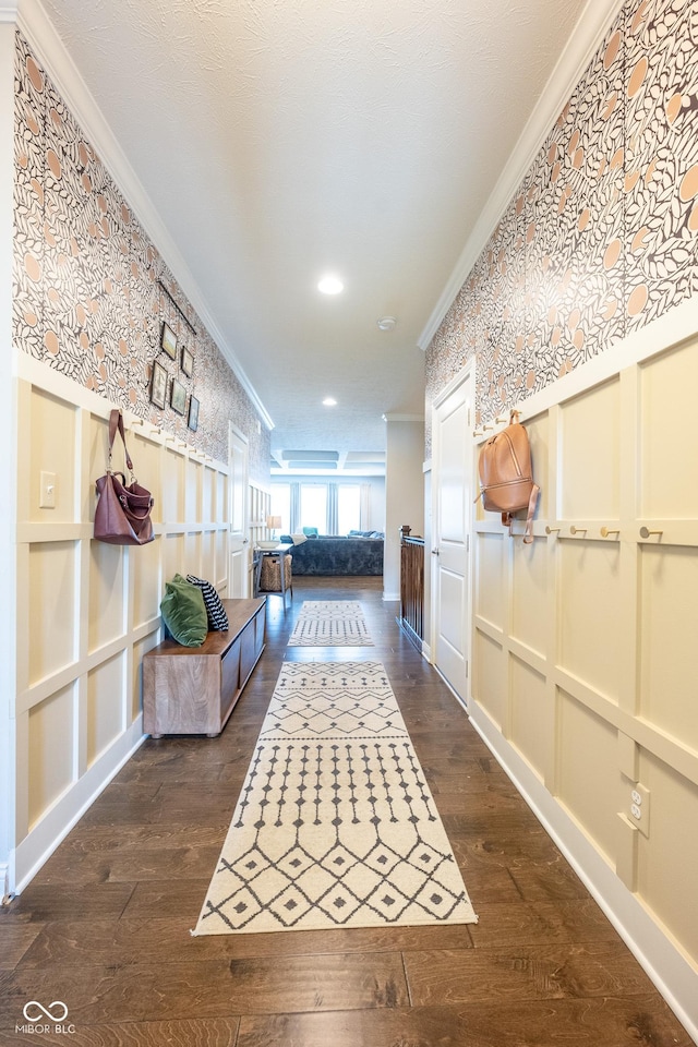 corridor featuring dark wood-type flooring, ornamental molding, a decorative wall, and wallpapered walls